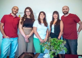 A team of five professional colleagues standing together in a modern office, showcasing their expertise and collaborative spirit.